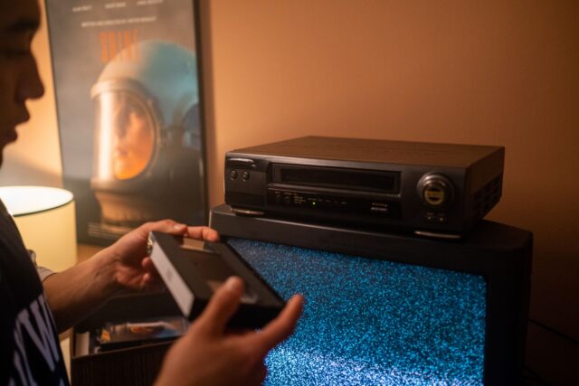 Stick de streaming conectat în portul HDMI al unui televizor, cu telecomanda așezată alături pe comodă